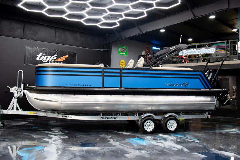 Slide: The Image of 2025 Viaggio Lago Z-U pontoon boat on trailer in showroom with modern lighting. - 2