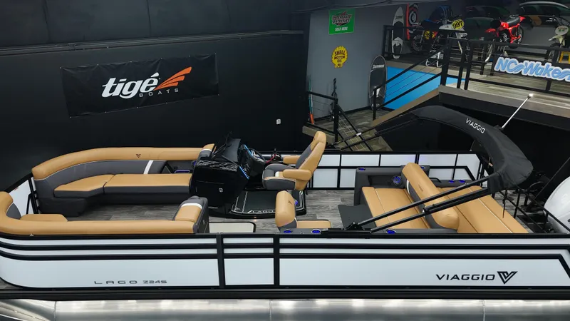 Slide: The Image of 2025 Viaggio Lago Z-S pontoon boat with tan seating and sleek design in showroom. - 17