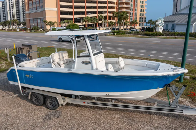 Slide: The Image of 2018 Sea Hunt 255 SE boat on trailer, parked near a road with buildings in the background. - 0