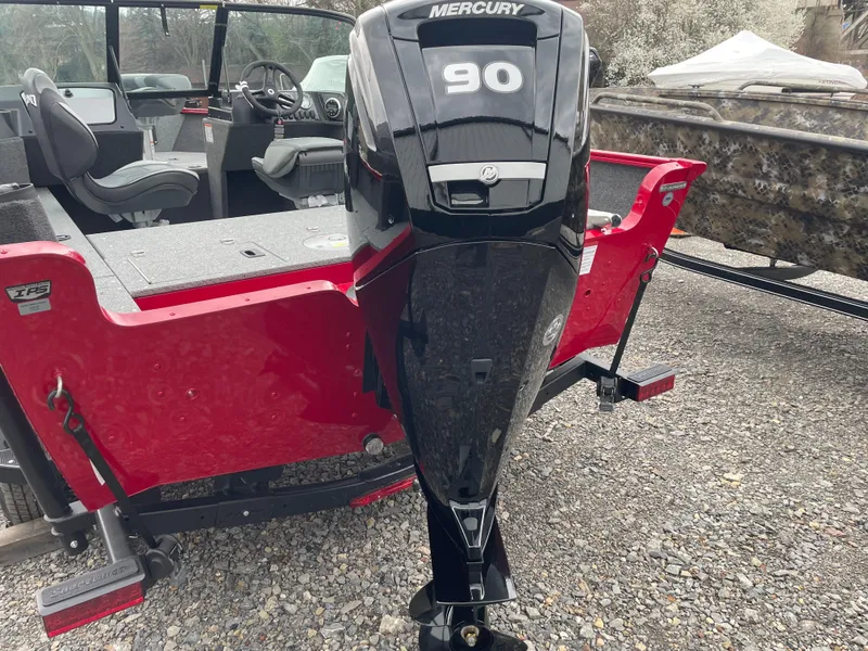 Slide: The Image of 2025 Lund 1650 Rebel XL Sport with Mercury 90 engine, red exterior, parked on gravel. - 12