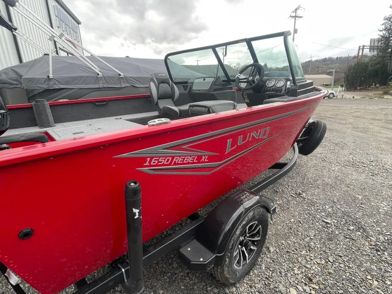 Slide: The Image of 2025 Lund 1650 Rebel XL Sport boat, red exterior, parked on gravel. - 19
