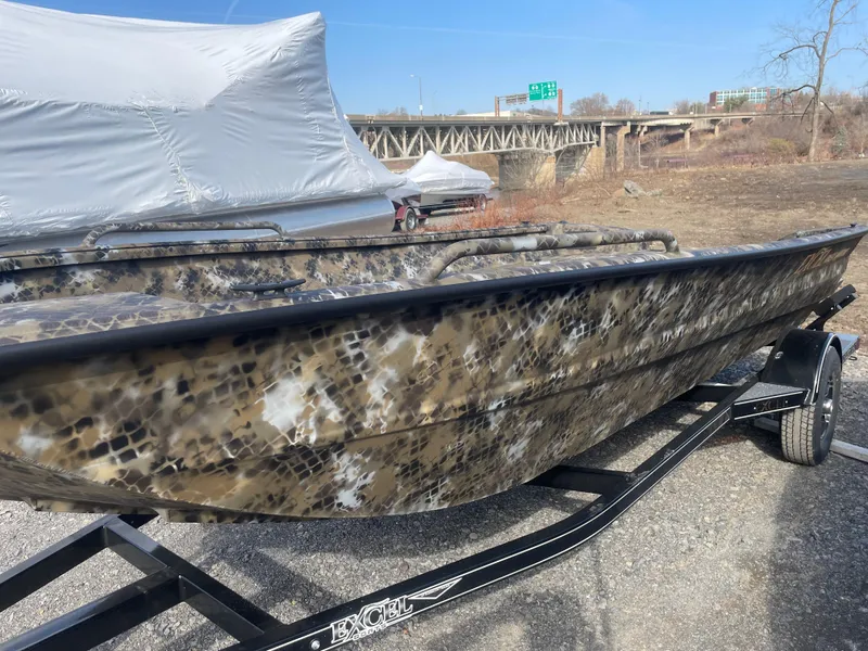 Slide: The Image of 2025 Excel 1751 River Warrior boat with camouflage design on a trailer, near a bridge. - 6