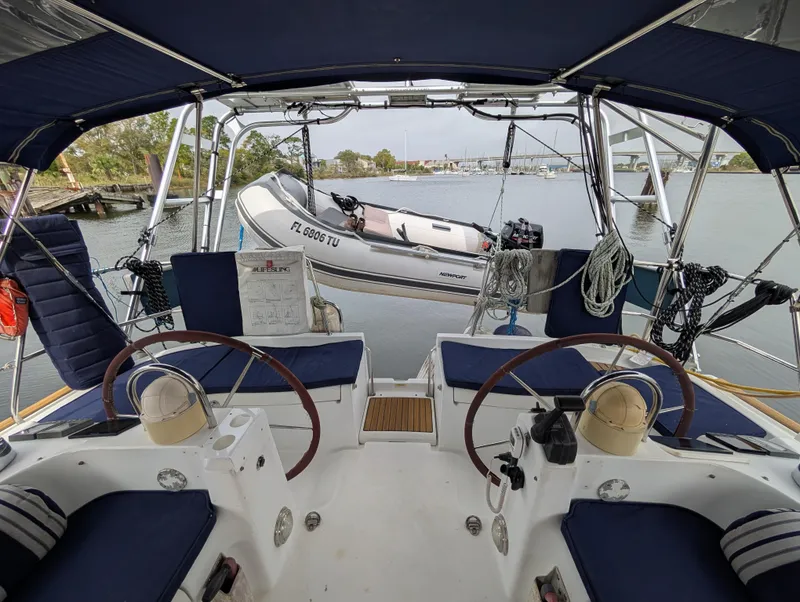 Slide: The Image of 2003 Beneteau Oceanis 473 cockpit with dual steering wheels and tender boat in background. - 28