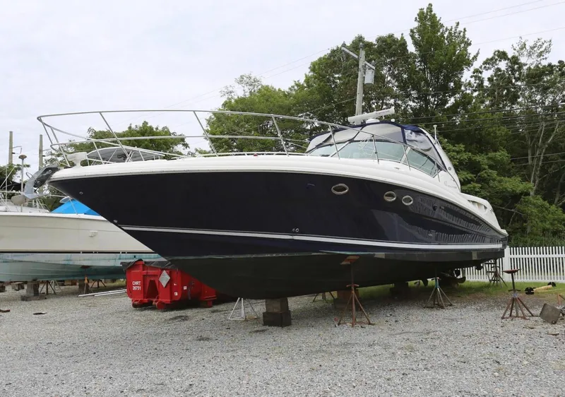 The Image of 2003 Sea Ray 420 Sundancer yacht on dry dock, surrounded by trees and gravel. - 0