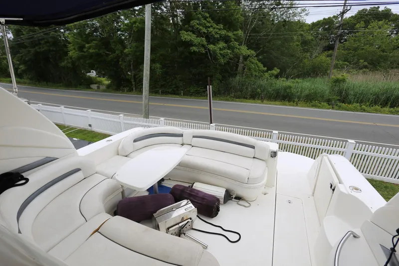 Slide: The Image of 2003 Sea Ray 420 Sundancer boat deck with white seating and table, near a road and greenery. - 23