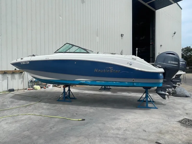 Slide: The Image of 2021 NauticStar 223 DC boat on stands, blue and white hull, Yamaha outboard motor. - 2