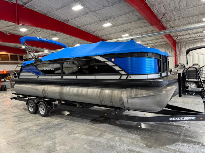 Slide: The Image of 2020 Godfrey 250 Monaco pontoon boat with blue cover on trailer in indoor storage. - 14