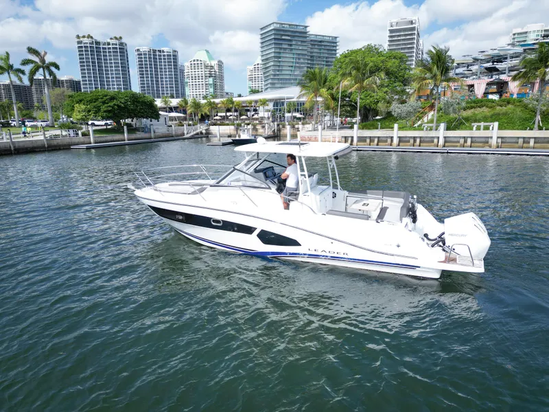 Slide: The Image of 2021 Jeanneau Leader 10.5 WA boat cruising in a marina with cityscape background. - 10