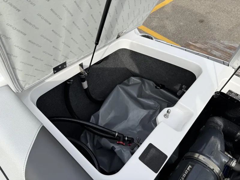 Slide: The Image of 2019 MasterCraft NXT22 storage compartment with open lid and visible hoses. - 18