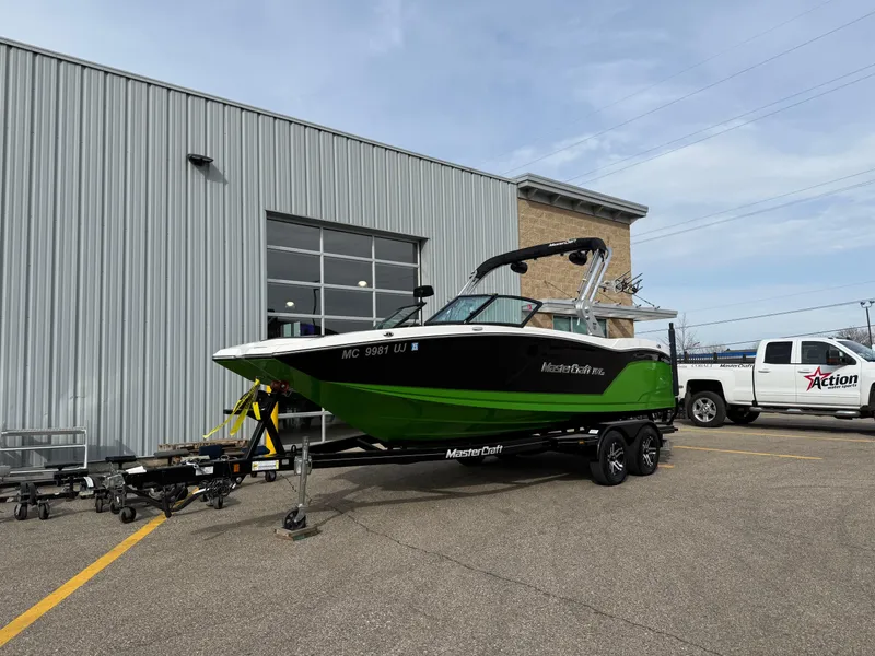 Slide: The Image of 2019 MasterCraft NXT22 boat on trailer outside dealership, with a white truck nearby. - 2