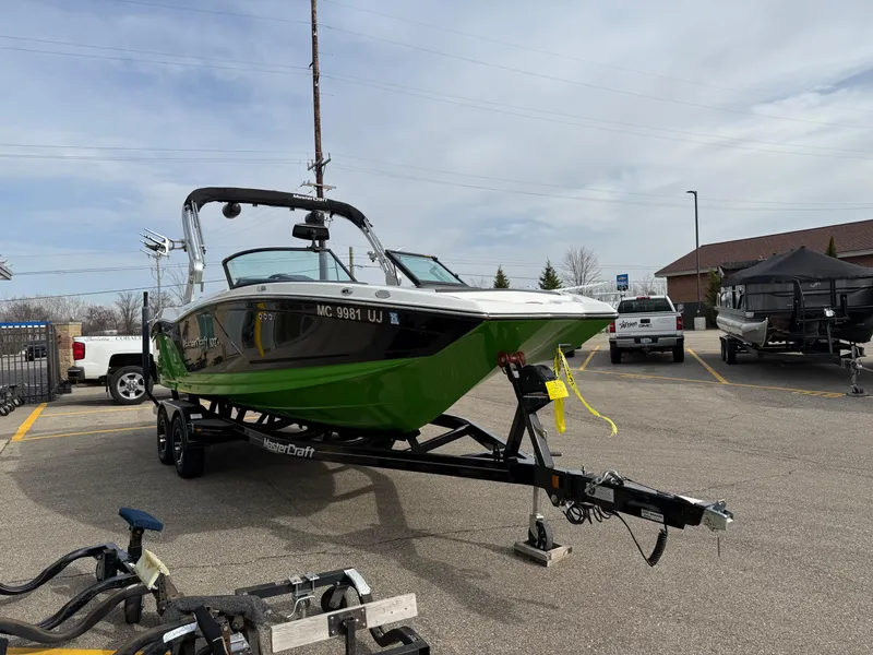Slide: The Image of 2019 MasterCraft NXT22 boat on trailer in parking lot, green and black design. - 6