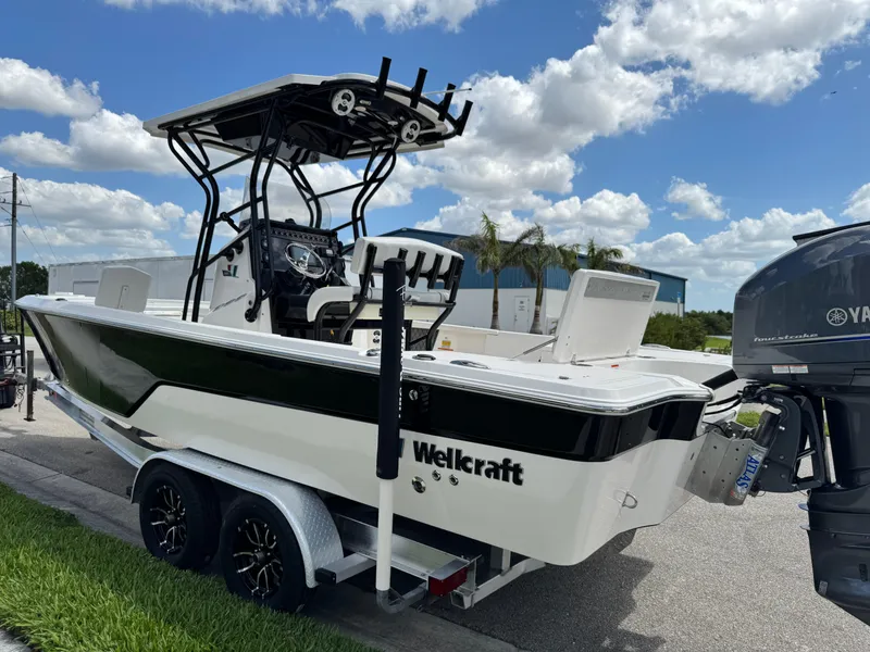 Slide: The Image of 2016 Wellcraft 241 boat on trailer, black and white design, parked outdoors under blue sky. - 16
