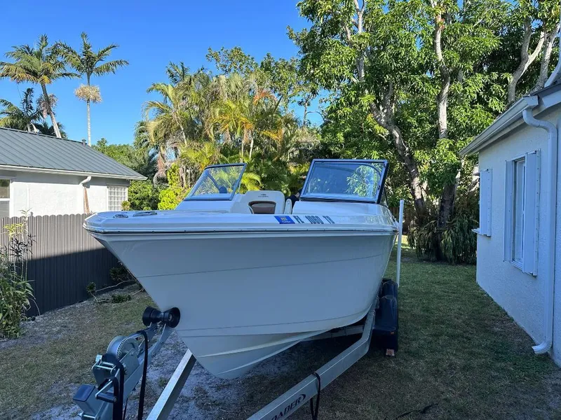 Slide: The Image of 2022 Cobia 220 DC boat on trailer, surrounded by tropical trees and house. - 2