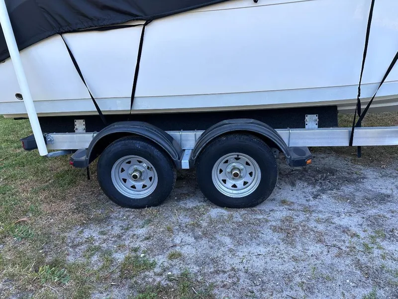 Slide: The Image of 2022 Cobia 220 DC boat on trailer with dual wheels, covered and parked on grass. - 23