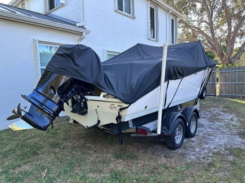 Slide: The Image of 2022 Cobia 220 DC boat covered on trailer, parked in a residential yard. - 5