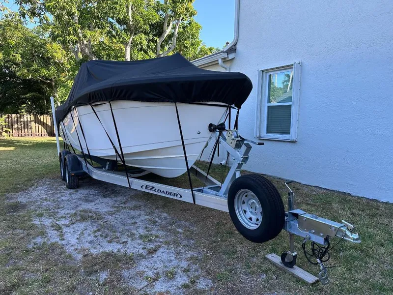Slide: The Image of 2022 Cobia 220 DC boat on trailer with cover, parked beside a house. - 6