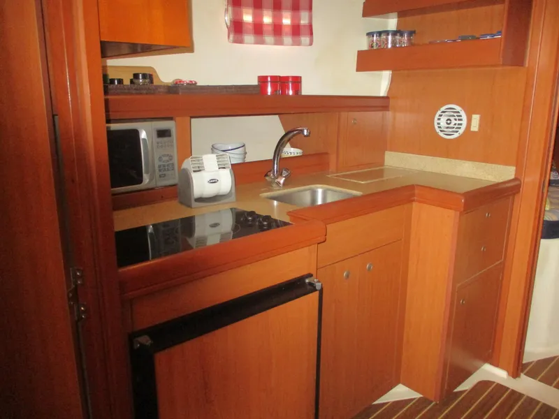 Slide: The Image of 2007 Mainship Pilot 34 Sedan kitchen with wood cabinetry, sink, microwave, and appliances. - 13