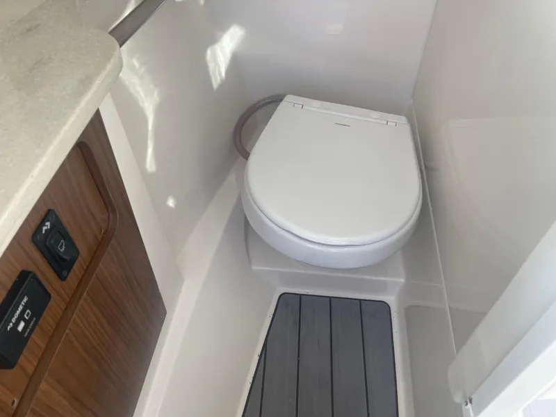 Slide: The Image of 2023 Sailfish 245 DC boat interior with compact marine toilet and wooden cabinetry. - 22