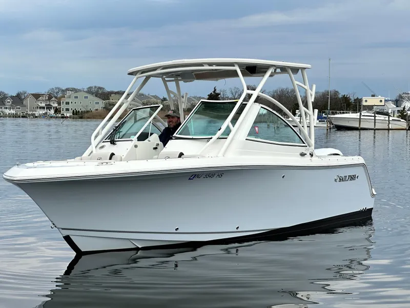 Slide: The Image of 2023 Sailfish 245 DC boat on calm water, with coastal houses in the background. - 6