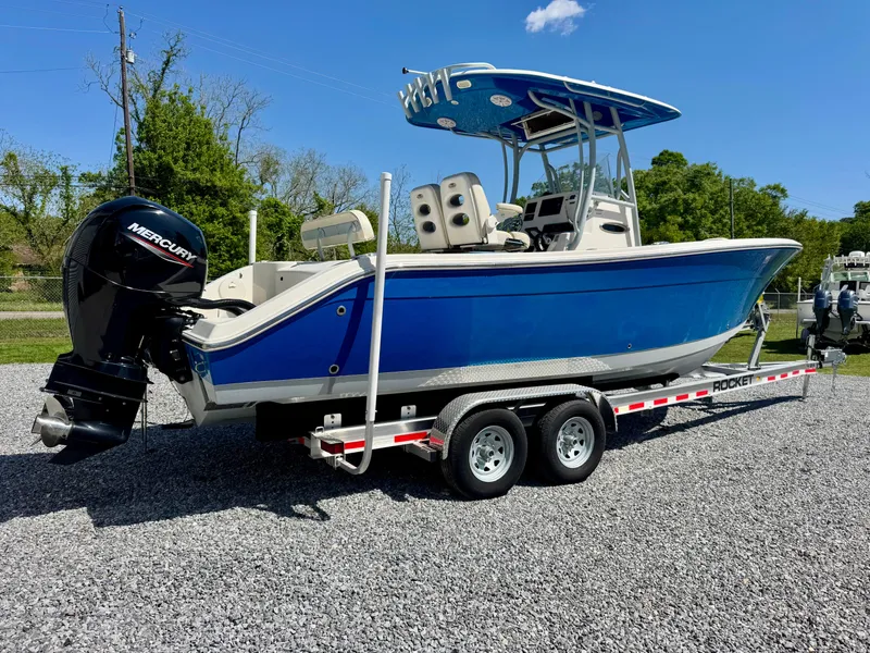 Slide: The Image of 2019 Cobia 261 boat on trailer, blue hull, Mercury outboard, parked on gravel. - 3