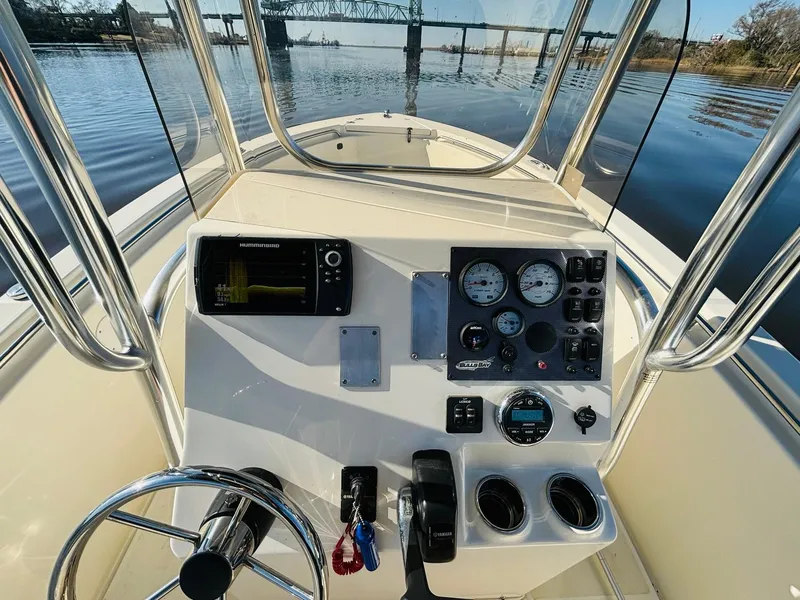Slide: The Image of 2017 Bulls Bay 230 Center Console boat dashboard with gauges and steering wheel on calm water. - 17