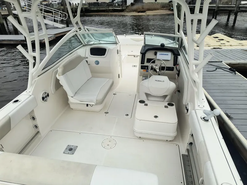 Slide: The Image of 2016 Robalo R247 Dual Console boat interior with seating and helm, docked by the water. - 5