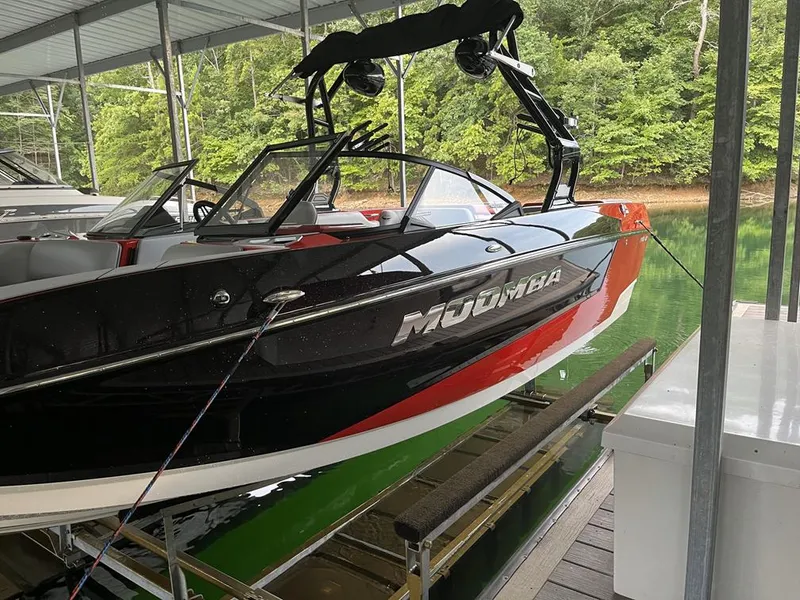 Slide: The Image of 2021 Moomba Mojo boat docked in a covered marina, surrounded by lush greenery. - 13