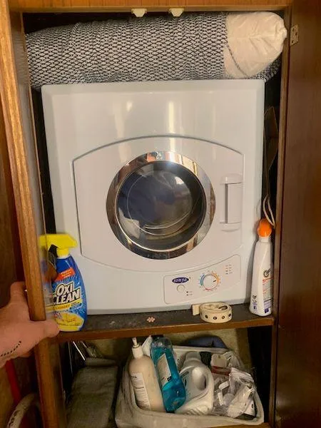 Slide: The Image of Compact washing machine in wooden cabinet with cleaning supplies and rolled mat on top. - 22