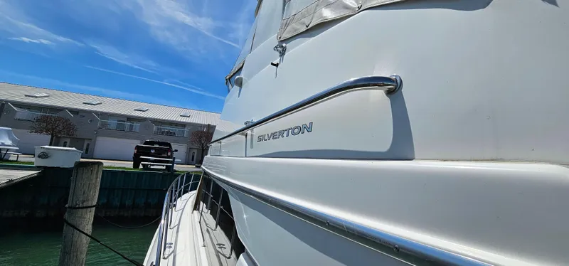 Slide: The Image of 2003 Silverton 42 Convertible yacht docked, showcasing sleek design and branding under a clear blue sky. - 14
