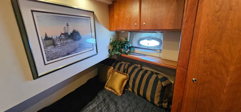 Slide: The Image of 2003 Silverton 42 Convertible cabin with cozy bed, striped pillows, and framed lighthouse artwork. - 46