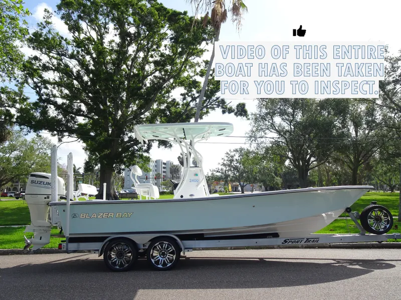 Slide: The Image of 2019 Blazer Bay 2400 boat on trailer, parked outdoors with trees in background. - 2