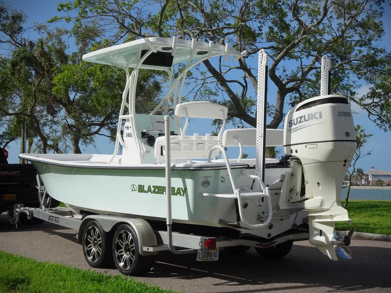 Slide: The Image of 2019 Blazer Bay 2400 boat on trailer with Suzuki engine, parked near trees and water. - 5