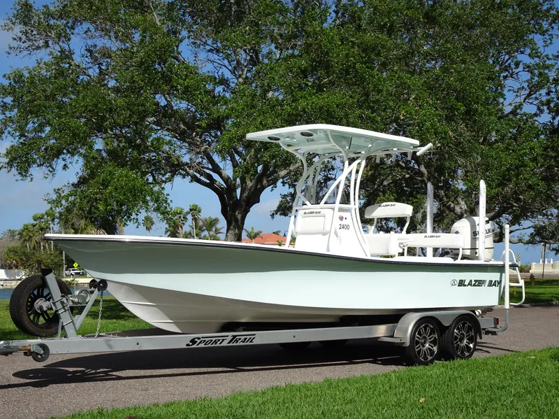 Slide: The Image of 2019 Blazer Bay 2400 boat on trailer, parked outdoors with trees in the background. - 7