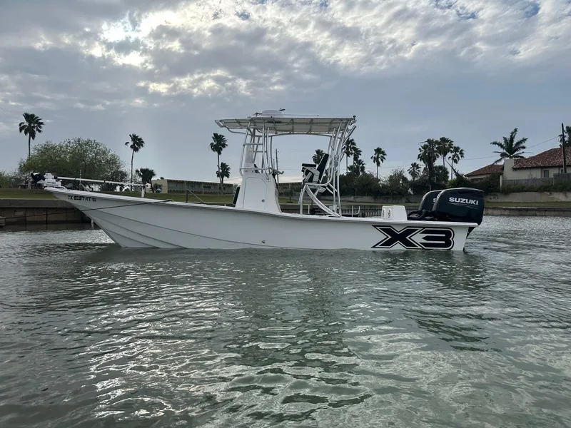 Slide: The Image of 2023 Shallow Sport 28 X3 boat on water, overcast sky, palm trees in background. - 24