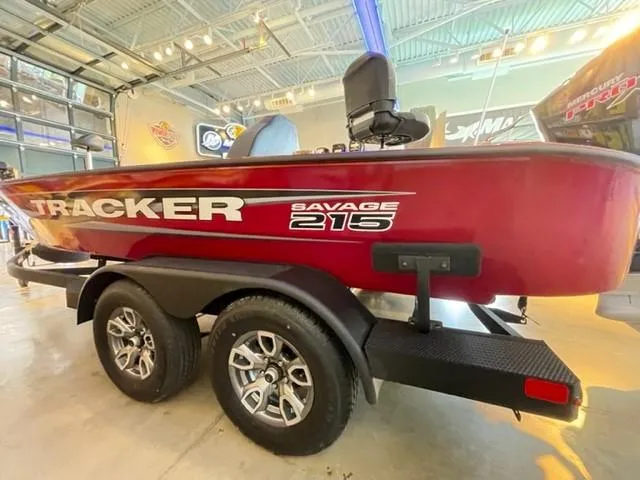 Slide: The Image of 2025 Tracker Savage 215 boat on trailer in showroom, red exterior, dual axles. - 2