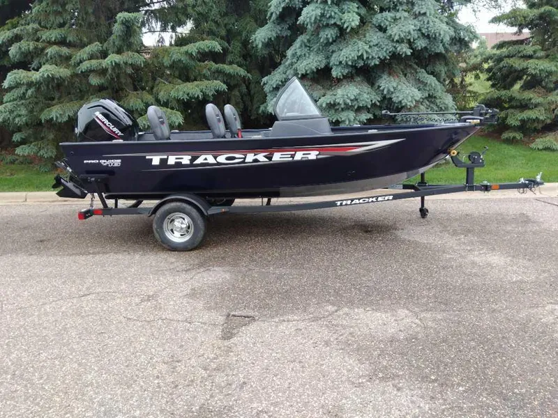 The Image of 2025 Tracker Pro Guide V-16 WT boat on trailer, parked near evergreen trees. - 0