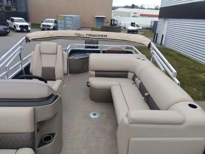 Slide: The Image of 2025 Sun Tracker Fishin' Barge 20 DLX with beige seating and canopy, parked outdoors. - 3