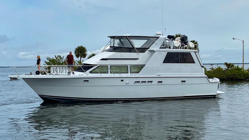 The Image of 1998 Hatteras 52 Cockpit Motor Yacht cruising on calm waters near lush greenery. - 0