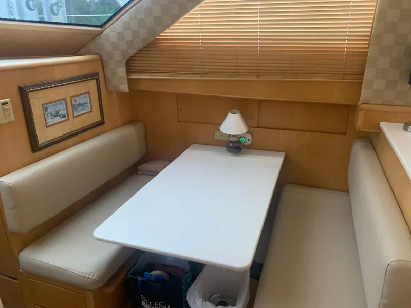 Slide: The Image of 1998 Hatteras 52 Cockpit Motor Yacht interior with dining area, beige seating, and table lamp. - 23