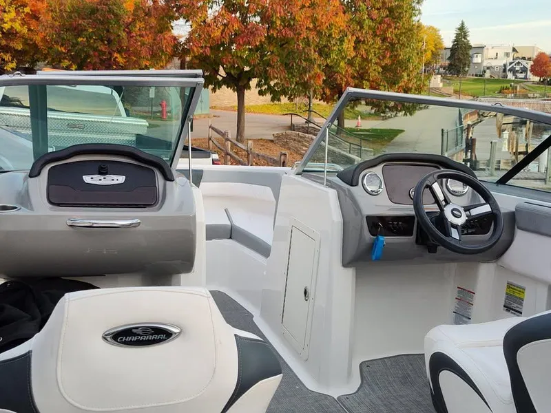 Slide: The Image of 2020 Chaparral 21 SSi OB boat interior with steering wheel, dashboard, and seating, docked near autumn trees. - 11
