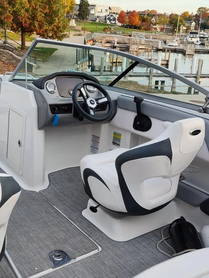 Slide: The Image of 2020 Chaparral 21 SSi OB boat interior with steering wheel and seating, docked by a marina. - 14