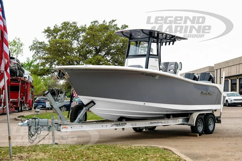 Slide: The Image of 2022 NauticStar 2602 Legacy boat on trailer, parked outdoors near trees and buildings. - 3