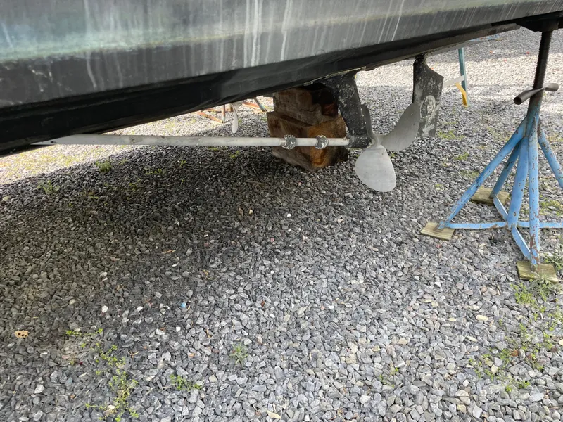 Slide: The Image of 1978 Bertram 33 Flybridge Cruiser propeller and hull on gravel with support stands. - 3