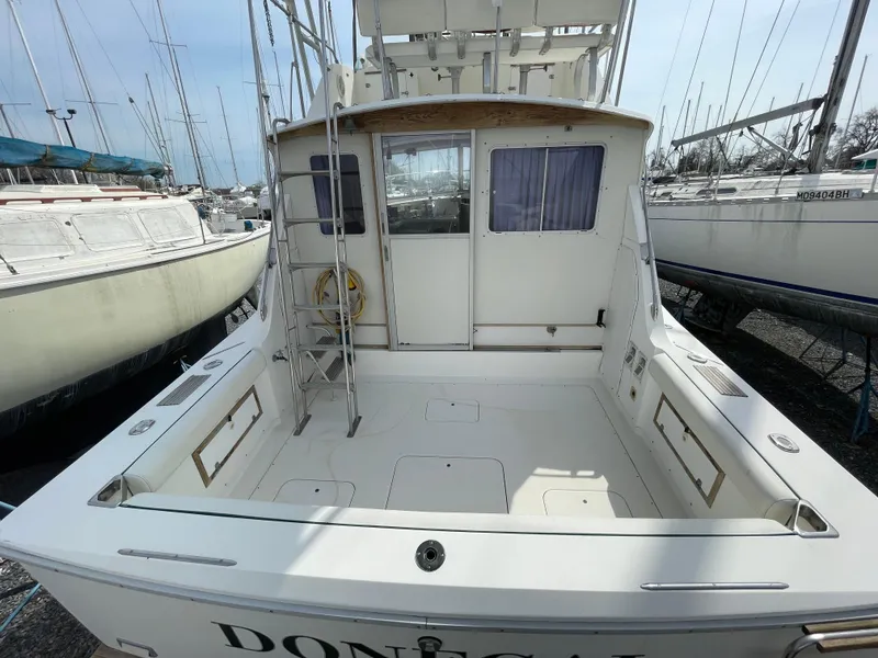 Slide: The Image of 1978 Bertram 33 Flybridge Cruiser, spacious deck, docked among other boats. - 7