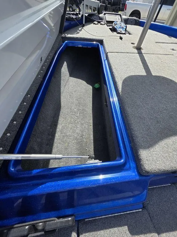 Slide: The Image of Open storage compartment in a 2016 Phoenix 819 Pro boat, featuring blue trim and carpeted interior. - 17