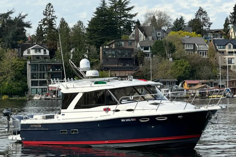 The Image of 2017 Cutwater C-302 Coupe boat on a scenic waterfront with houses and trees. - 0