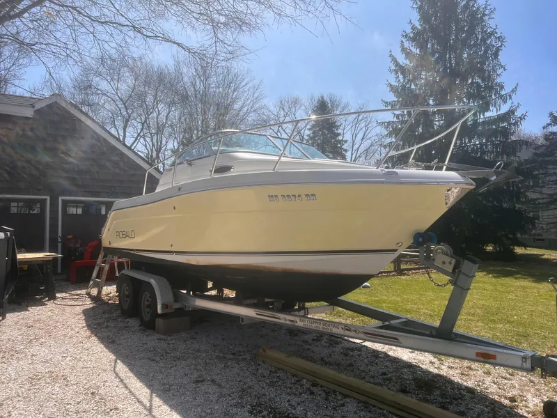 The Image of 2004 Robalo R225 Walkaround boat on trailer, parked outdoors near a garage. - 0