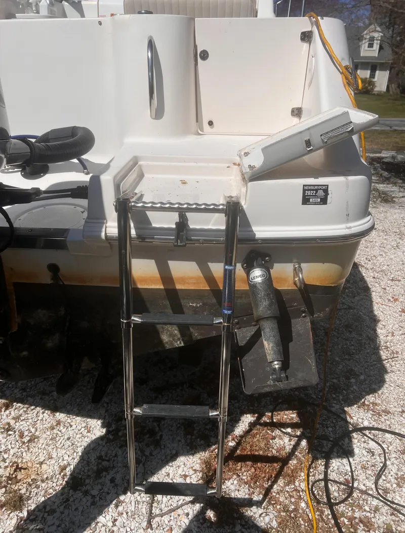 Slide: The Image of 2004 Robalo R225 Walkaround boat with ladder and motor, parked on gravel. - 13