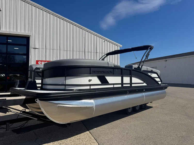 Slide: The Image of 2025 Bennington 22 MFB pontoon boat parked outside a warehouse on a sunny day. - 1