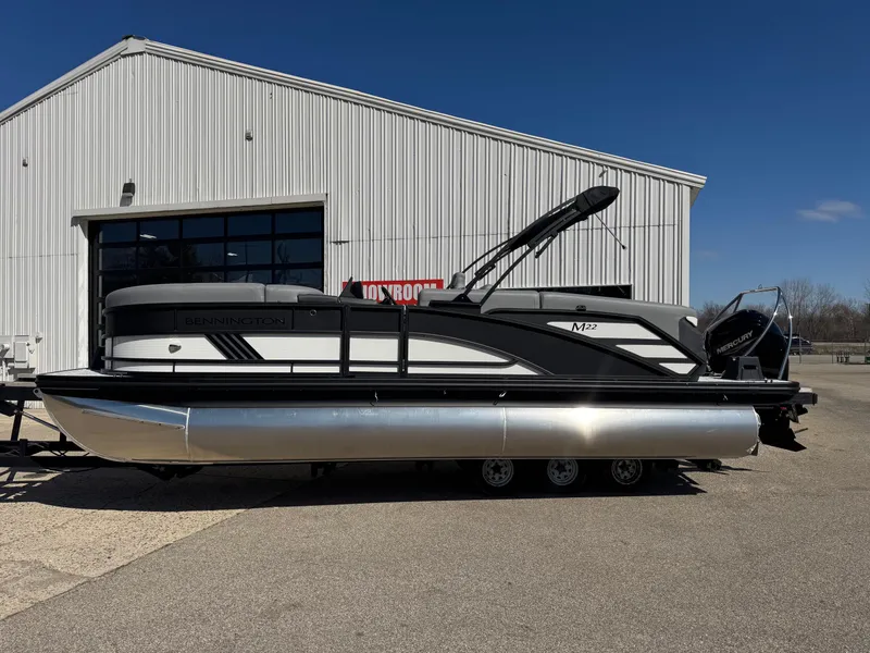 Slide: The Image of 2025 Bennington 22 MFB pontoon boat parked outside a large white building. - 2